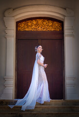 Obraz premium Graceful woman elegant white gown with long flowing train stands stone steps front of large wooden door with ornate golden decoration