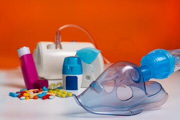 Face mask of modern nebulizer on white table. Equipment for inhalation, close-up, selective focus, orange background. Asthma breathing treatment. Bronchitis, asthmatic health equipment.