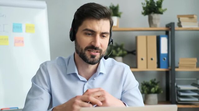 Caucasian man with headset during video call in bright office with plants and whiteboard. Natural lighting highlights the professional workspace.