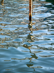 A wooden pole, water, sun, and reflections as abstract artists.