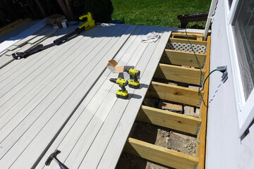 Deck boards partially installed over wooden joists on new deck foundation with power tools on planks