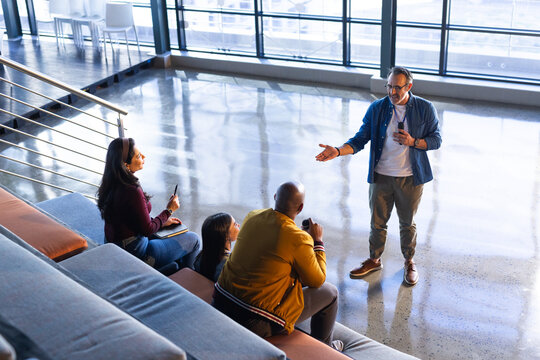 Diverse coworkers holding travel mug listening to presenter using headset mic in lounge, copy space