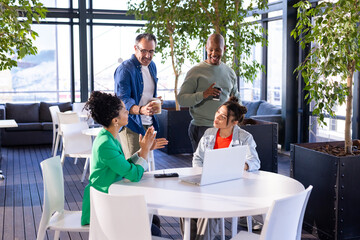 Diverse coworkers in business wear gathering in lounge using laptop remote control with coffee mugs