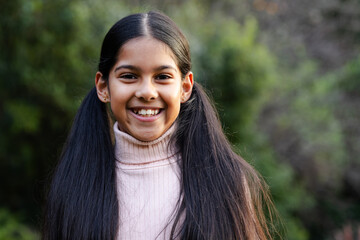 Indian girl child smiling, wearing pastel pink turtleneck sweater with earrings in garden