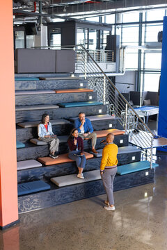 Diverse coworkers engaging in presentation on mezzanine with microphones, staircase, copy space