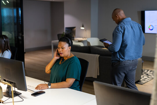 Diverse coworkers working at open-plan office using monitors, keyboard and tablet with charts