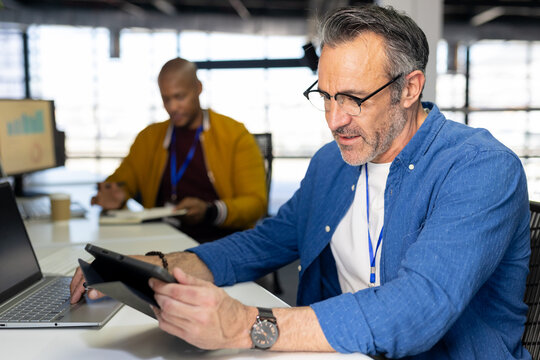 Diverse male colleagues studying tablet and writing in notebook in office near blinds, copy space