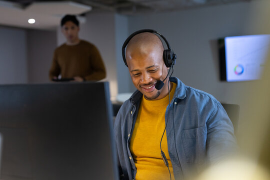 Diverse coworkers speaking into headset and using tablet at modern office with screen, copy space