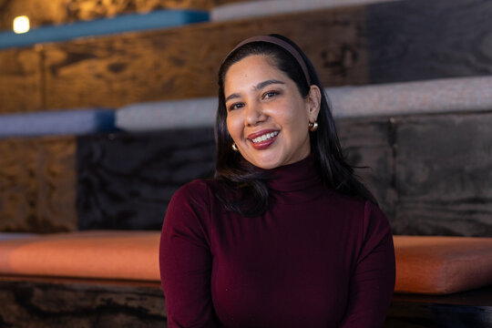 Mid adult woman sitting on tiered benches with cushions in hall wearing maroon headband and smiling