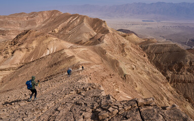 Unique landscape in Eilat Mountains nature reserve, the southern Negev, as seen from the Israel Trail passes through the reserve. A group of hikers descending along a mountain ridge. Active lifestyle.