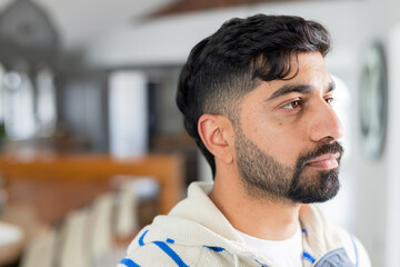 Indian man standing in modern home kitchen area wearing white and blue striped hoodie, copy space