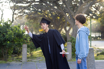 Diverse friends celebrating graduation on park walkway holding diploma scroll and flicking tassel