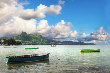 Traditional boats floating in a calm lagoon with green mountains and tropical clouds, Mauritius, Indian Ocean