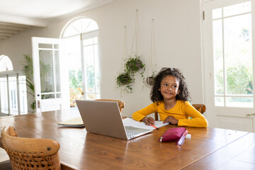 African American girl sitting at home writing with red pencil on paper near laptop, copy space