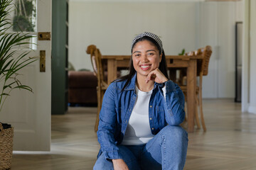 Kneeling woman wearing denim jacket and headband in dining area near wooden table and woven basket