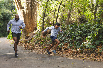 African American father and son jogging through park path passing leaves on ivy-covered pavement