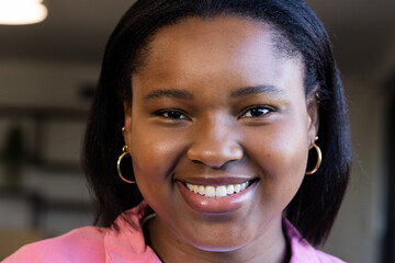 African American woman smiling into camera wearing pink blouse and gold hoop earrings in office