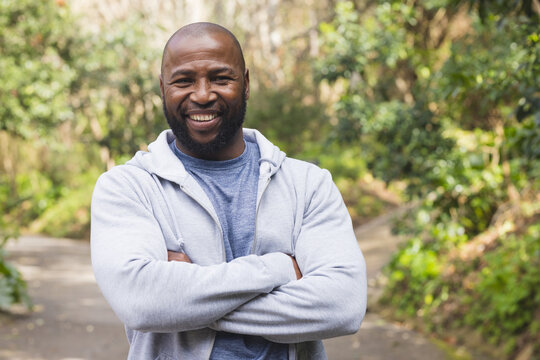 African American man standing on sunlit forest path wearing gray hoodie over blue t-shirt smiling