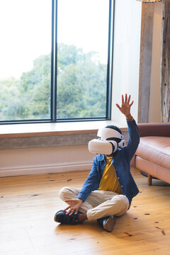 Virtual reality headset is enabling immersive gestures on wood floor near window, brown sofa behind