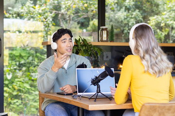 Diverse podcast hosts recording at wooden table in home studio with laptop, microphones