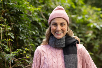 Female standing on park path wearing pink beanie, cable-knit sweater and grey-and-black scarf