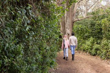 Couple walking along narrow dirt trail in park wearing pink knit beanie, gray scarf, rubber boots