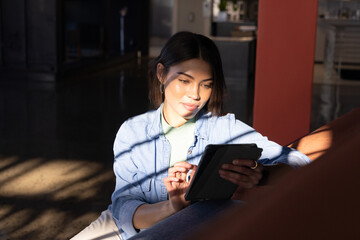 Asian Indian woman sitting on denim sofa using tablet in modern lounge with red column