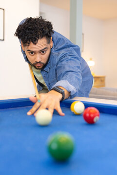 Man leaning over pool table in game room aiming cue ball with cue stick among balls