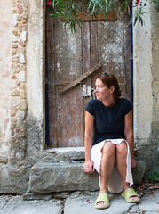 A cheerful woman sits on the steps of an old rustic house