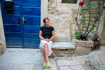 A cheerful woman sits on the steps of an old rustic house