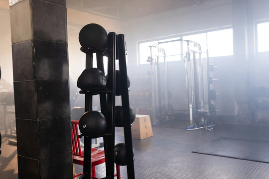 Vertical medicine ball rack is holding numbered black balls in gym near column and red chair