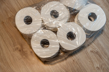 Rolls of toilet paper packaged in plastic on a wooden floor, highlighting everyday household essentials for hygiene and comfort. Ideal for home supply advertisements, marketing, or product listings.