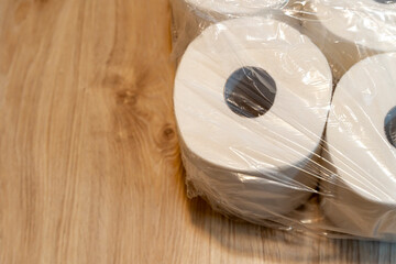 Pack of white toilet paper rolls wrapped in plastic on a wooden surface, offering a clean and simple composition for hygiene and home essentials marketing.