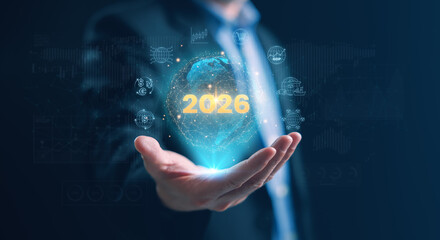 A businessman holding a glowing holographic globe with 2026 and global economy icons, symbolizing worldwide market trends, currency exchange, trade, logistics, and economic growth insights for 2026.