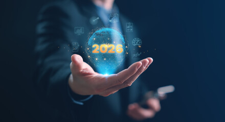 A businessman holding a glowing holographic globe with 2026 surrounded by KPI, performance, and analytics icons, representing future business performance, data tracking, and strategic growth in 2026.
