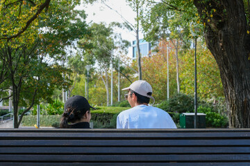 A couple sitting in a city park, spending time together in a peaceful outdoor environment with green trees and natural light.