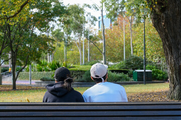 A couple sitting in a city park, spending time together in a peaceful outdoor environment with green trees and natural light.