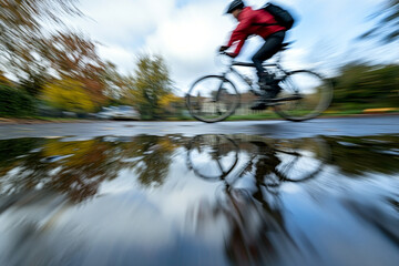 Naklejka premium cyclist motion blur reflected in puddle after rainfall