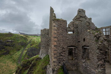Ruins of Dunluce Castle in Northern Ireland, with the remains of its stone walls and towers standing under a cloudy sky, highlighting its medieval architecture.