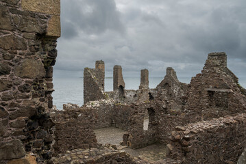 Ruins of Dunluce Castle in Northern Ireland, with the remains of its stone walls and towers standing under a cloudy sky, highlighting its medieval architecture.