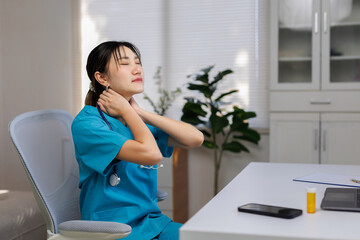 Young nurse wearing scrubs and a stethoscope, feeling tired and stressed, rubbing aching neck and shoulder muscles