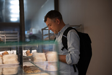 Person standing near pastry display checking phone in bakery environment
