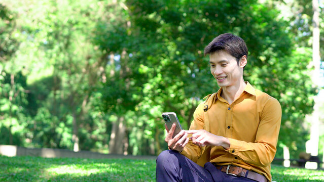 Young asian businessman using smartphone outdoors in park