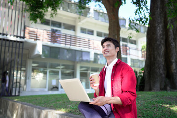 Man working remotely outdoors, drinking coffee and using laptop in city park