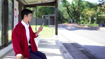 Young man with smartphone waiting for public transport at bus stop