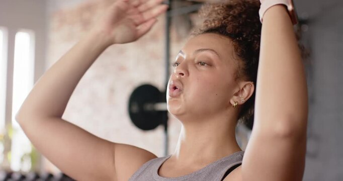 Locking hands behind head in front of dumbbell rack, woman performing breathing exercises for focus