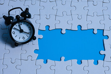 Problem solving concept with a black alarm clock placed on an incomplete puzzle revealing blue...
