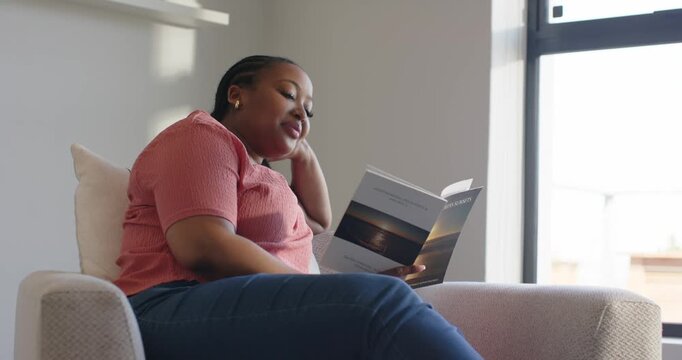 Grasping travel brochure woman flipping pages in chair at home by window while planning trip