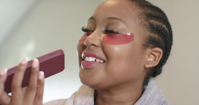 African American woman at vanity adjusting phone angle, showing pink gel patches for skincare
