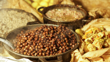 Steaming outdoor feast featuring a cast iron skillet with peas, beans, greens, and barley grains and potatoes. Cooked over an open flame. Warm, rustic even medieval communal and inviting atmosphere.